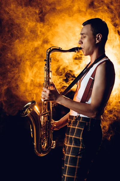 Vista lateral del expresivo y elegante joven músico tocando el saxofón en el humo — Stock Photo