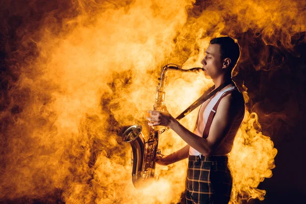 Vista lateral del expresivo y elegante joven jazzman tocando el saxofón en el humo — Stock Photo