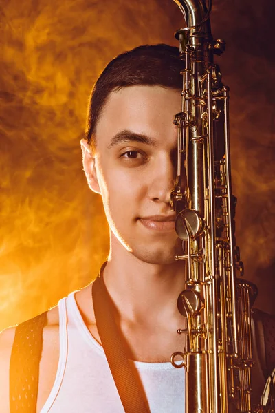 Primer plano vista de guapo joven músico con saxofón sonriendo a la cámara - foto de stock