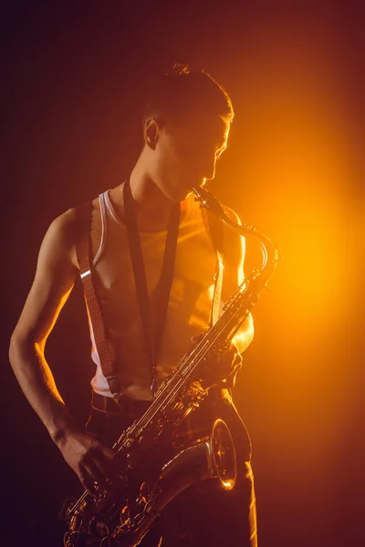 Hermoso joven jazzman jugando saxofón contra foco - foto de stock