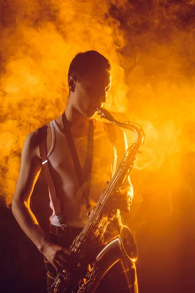 Apuesto joven músico tocando saxofón en el humo — Stock Photo