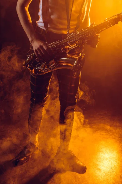 Low section of young musician holding saxophone in smoke — Stock Photo