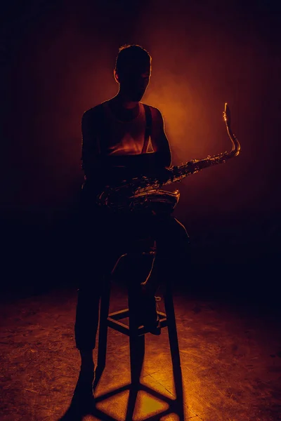 Силует молодого саксофоніста, що сидить на табуреті з саксофоном — стокове фото