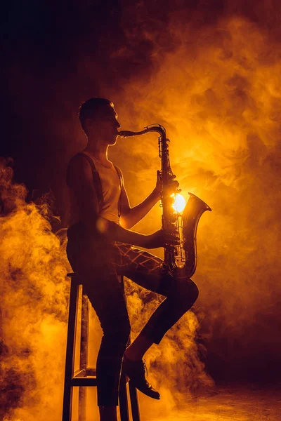 Young expressive jazzman sitting on stool and playing saxophone — Stock Photo