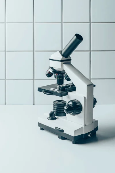 Microscopio óptico moderno en tableta blanca delante de la pared de azulejos - foto de stock