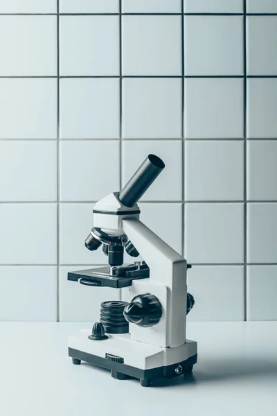 Microscope optique sur tablette blanche devant la paroi carrelée — Photo de stock