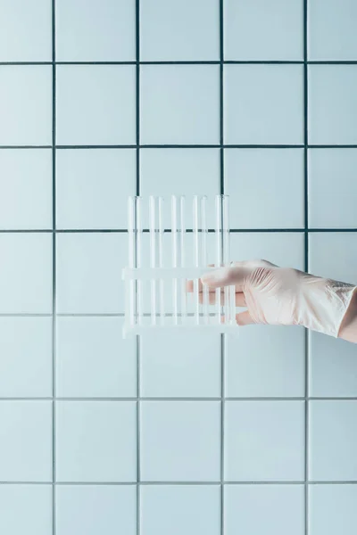 Cropped shot of doctor in glove holding test tubes in stand in front of tiled white wall — Stock Photo