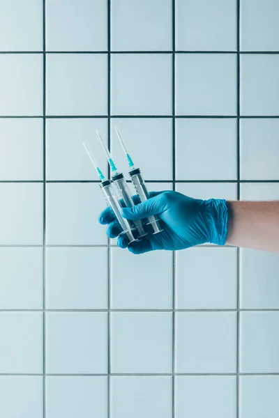 Cropped shot of doctor in glove holding syringes in front of tiled white wall — Stock Photo