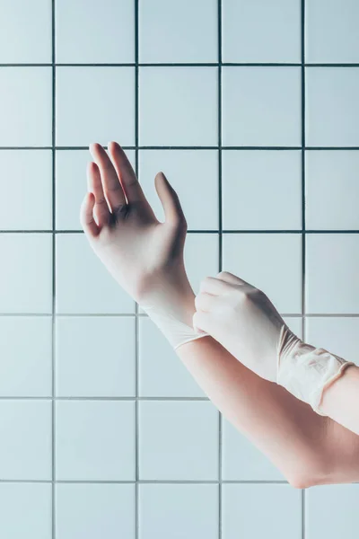 Tiro recortado de médico poner guantes de goma delante de la pared blanca de azulejos - foto de stock