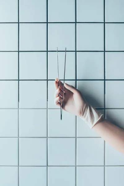 Tiro cortado de médico em luva segurando pinças na frente da parede branca de azulejos — Fotografia de Stock