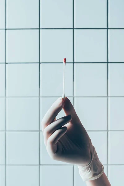 Tiro recortado do doutor na luva que prende o cotonete com sangue com líquido transparente na frente da parede branca telhada — Fotografia de Stock