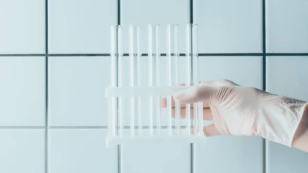 Foto recortada de médico sosteniendo tubos de ensayo en pie frente a la pared blanca de azulejos - foto de stock