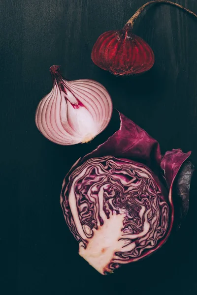 Vista superior de las mitades de remolacha, cebolla y col roja sobre una mesa gris oscura - foto de stock