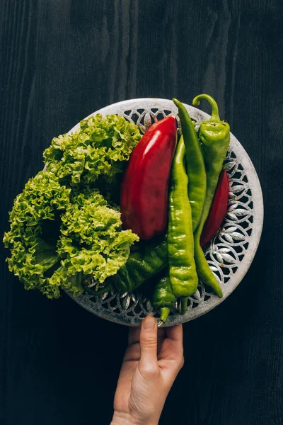 Cropped image of woman holding plate with green salad and chili peppers — Stock Photo