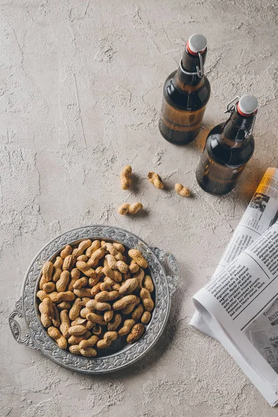 Vue de dessus des bouteilles de bière, cacahuètes et journaux disposés sur table en béton — Photo de stock