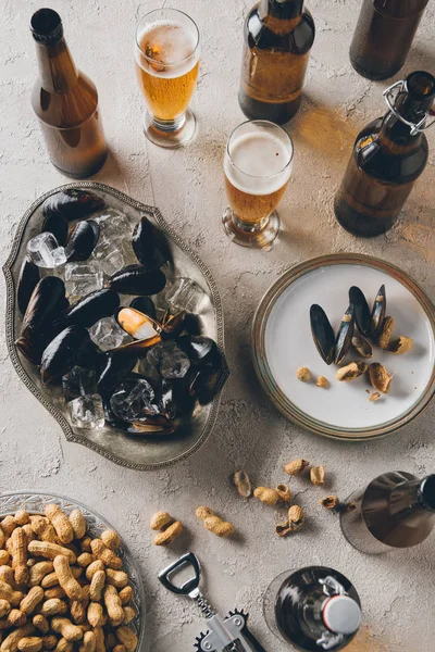 Vista superior de amendoins, mexilhões com cubos de gelo e cerveja fria dispostos em mesa de concreto — Fotografia de Stock