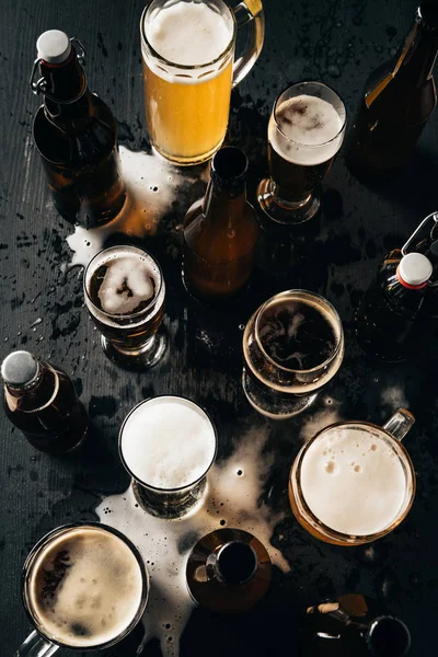 Top view of arrangement of bottles and glasses of beer on dark wooden tabletop — Stock Photo