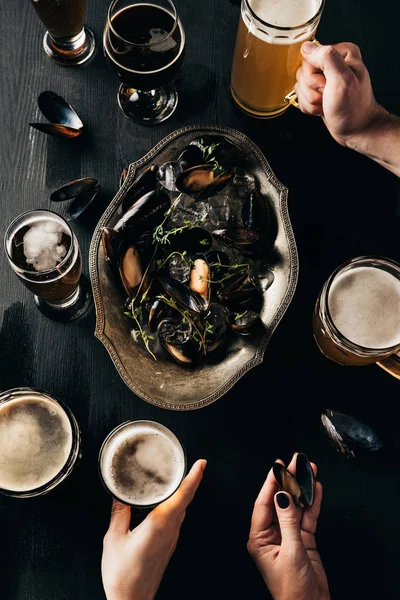 Partial view of friends with glasses of beer at tabletop with mussels in bowl — Stock Photo