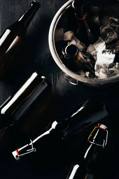 Flat lay with bucket, bottles of beer and ice cubes arranged on dark tabletop — Stock Photo