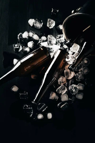 Flat lay com balde, garrafas de vidro de cerveja e cubos de gelo dispostos em mesa escura — Fotografia de Stock