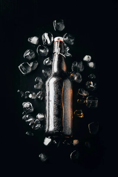 Flat lay with glass bottle of beer on ice cubes arranged on dark tabletop — Stock Photo