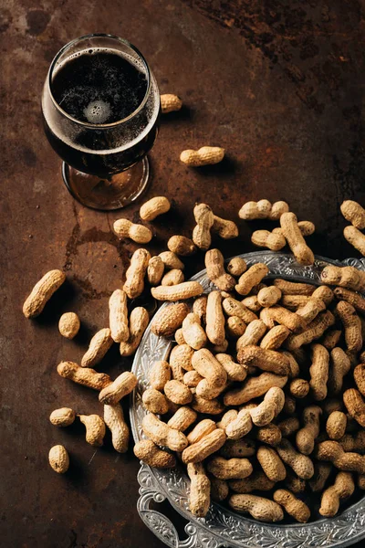 Vista superior de taza de cerveza fría y cacahuetes en bandeja de metal en la mesa oxidada - foto de stock