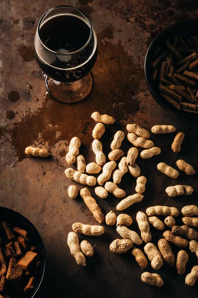 Top view of peanuts, baked breads and glass of beer on rust tabletop — Stock Photo