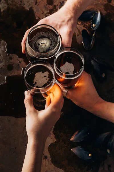 Tiro cortado de amigos latejando canecas de cerveja na superfície escura — Fotografia de Stock