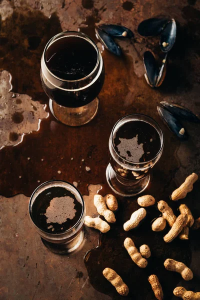 Vue de dessus des verres de bière froide, cacahuètes et coquilles de moules sur la surface de la rouille — Photo de stock