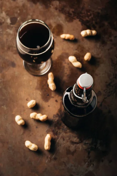 Top view of arranged peanuts, bottle and glass of beer on rust tabletop — Stock Photo