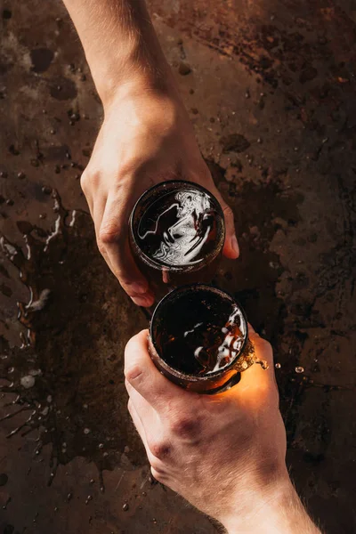 Tiro cortado de amigos latejando canecas de cerveja na superfície escura — Fotografia de Stock