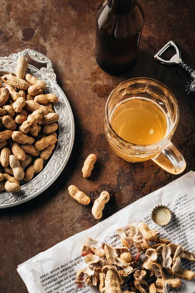 Top view of arranged glass and bottle of beer, newspaper and peanuts on tray on rust surface — Stock Photo