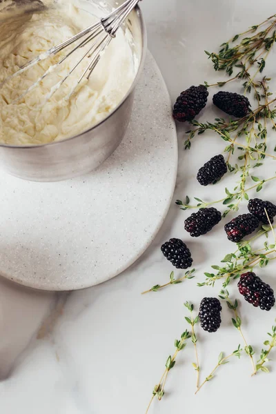 Cropped shot of bowl with whisk and cream for cake and blackberries on white table — Stock Photo