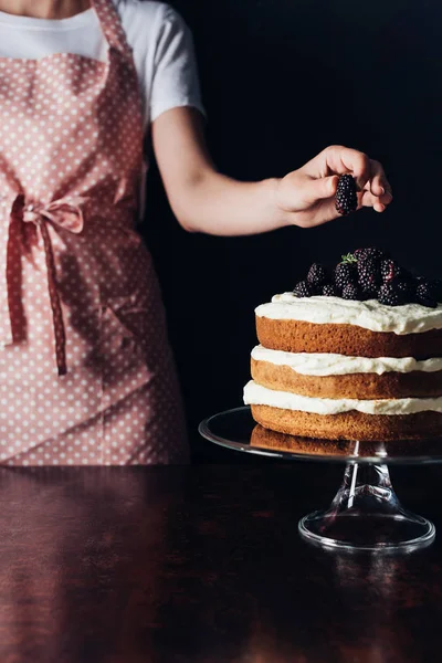 Tiro recortado de mujer decorando pastel de mora recién horneado en soporte de vidrio en negro — Stock Photo