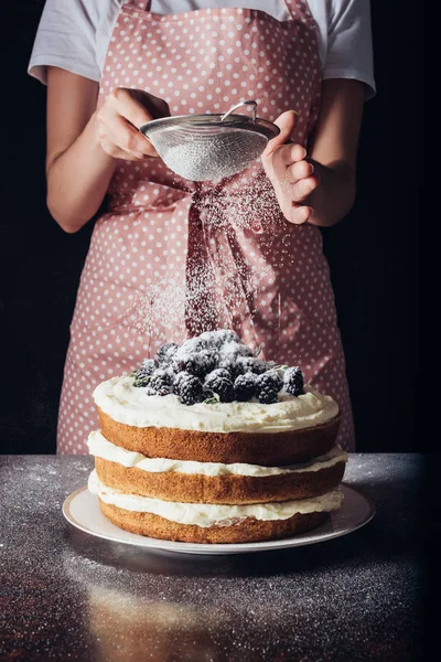 Cropped shot of woman spilling sugar powder onto tasty blackberry on black — Stock Photo