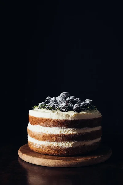 Gros plan d'un délicieux gâteau aux mûres sur une planche à découper en bois et sur du noir — Photo de stock