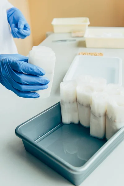 Partial view of biologist in latex gloves putting paper with seeds in agro laboratory — Stock Photo