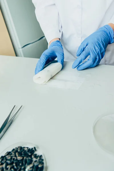 Vista parcial del científico en guantes de látex trabajando en la mesa en laboratorio moderno - foto de stock