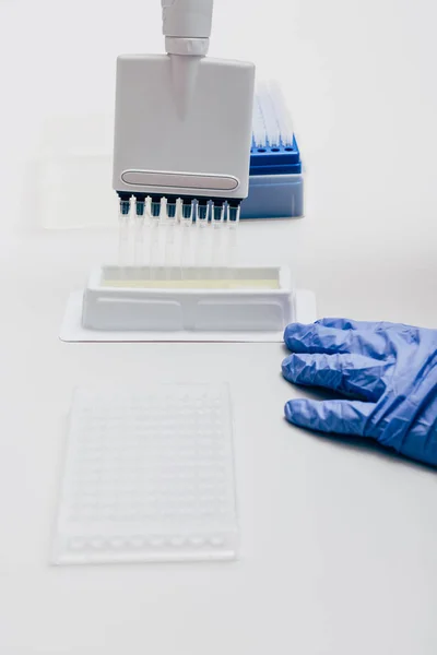 Imagen recortada del científico utilizando pipeta multicanal en mesa de trabajo con frascos en laboratorio de biotecnología - foto de stock