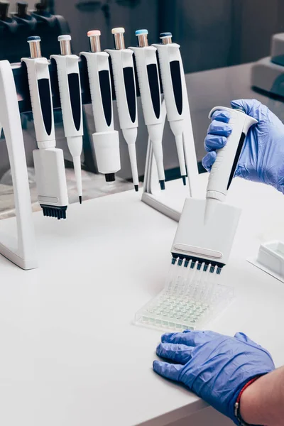 Partial view of scientist using multichannel pipette at working table with flasks in modern laboratory — Stock Photo