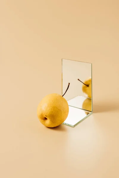 Вкусная желтая груша, отражающаяся в двух зеркалах на бежевом столе — стоковое фото