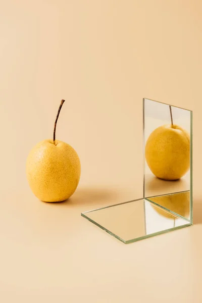 Pera amarilla orgánica reflejándose en dos espejos sobre mesa beige - foto de stock