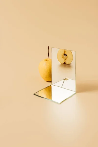 Apetecible pera amarilla que se refleja en dos espejos en la mesa beige - foto de stock