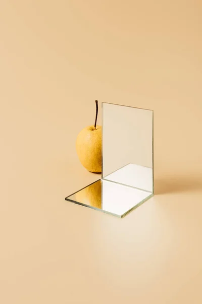 Pera amarilla y dos espejos sobre mesa beige - foto de stock