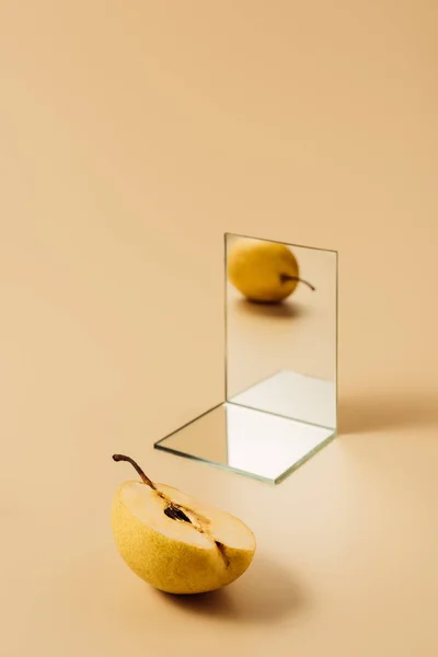 Una pera amarilla que se refleja en dos espejos sobre una mesa beige - foto de stock