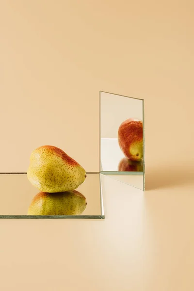 Yellow pear reflecting in two mirrors on beige table — Stock Photo