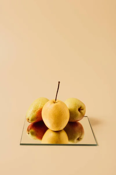 Tres peras en el espejo en la mesa beige - foto de stock
