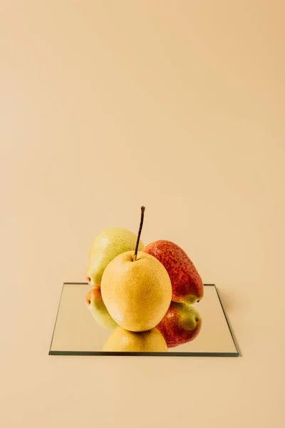 Three pears reflecting in mirror on beige table — Stock Photo