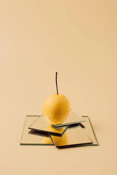 Una pera amarilla en espejos sobre mesa beige - foto de stock