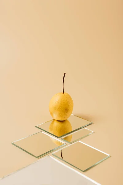 Желтая груша отражается в зеркалах на бежевой поверхности — стоковое фото